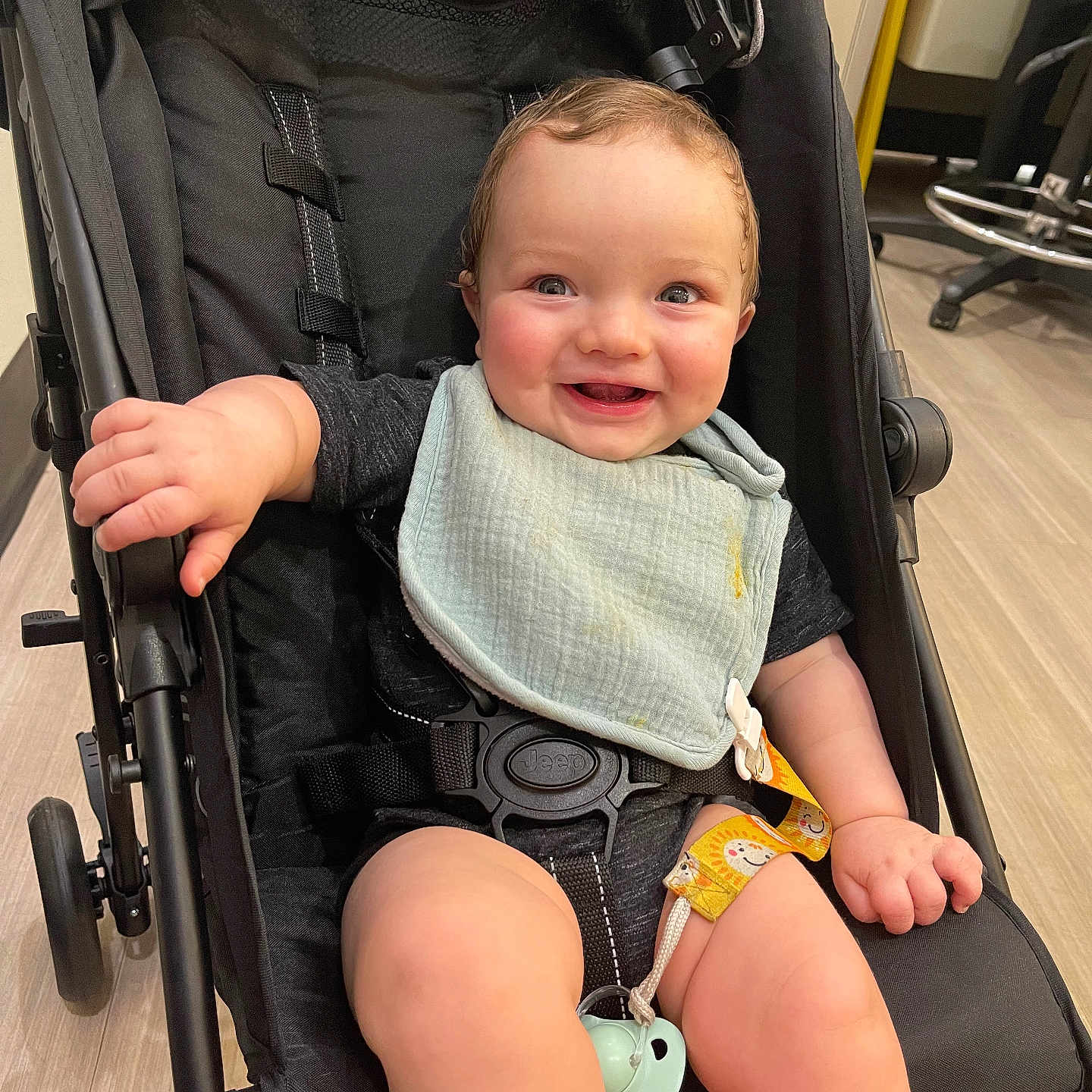 Jaxxon joined the competition — help win amazing prizes! baby, bib, black_stroller, child, clothing, cute, face, floor, hand, happy, indoor, infant, legs, pacifier, seatbelt, sitting, smiling, stroller, toy, wooden_floor
