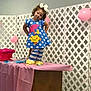 Jayden is registered to the contest to win money with this photo: child, girl, blue_dress, polka_dots, bow, curly_hair, table, pink_cloth, balloons, indoor, party, lattice_fence, striped_leggings, yellow_socks, cute, playful, posing, festive, decorations, smile