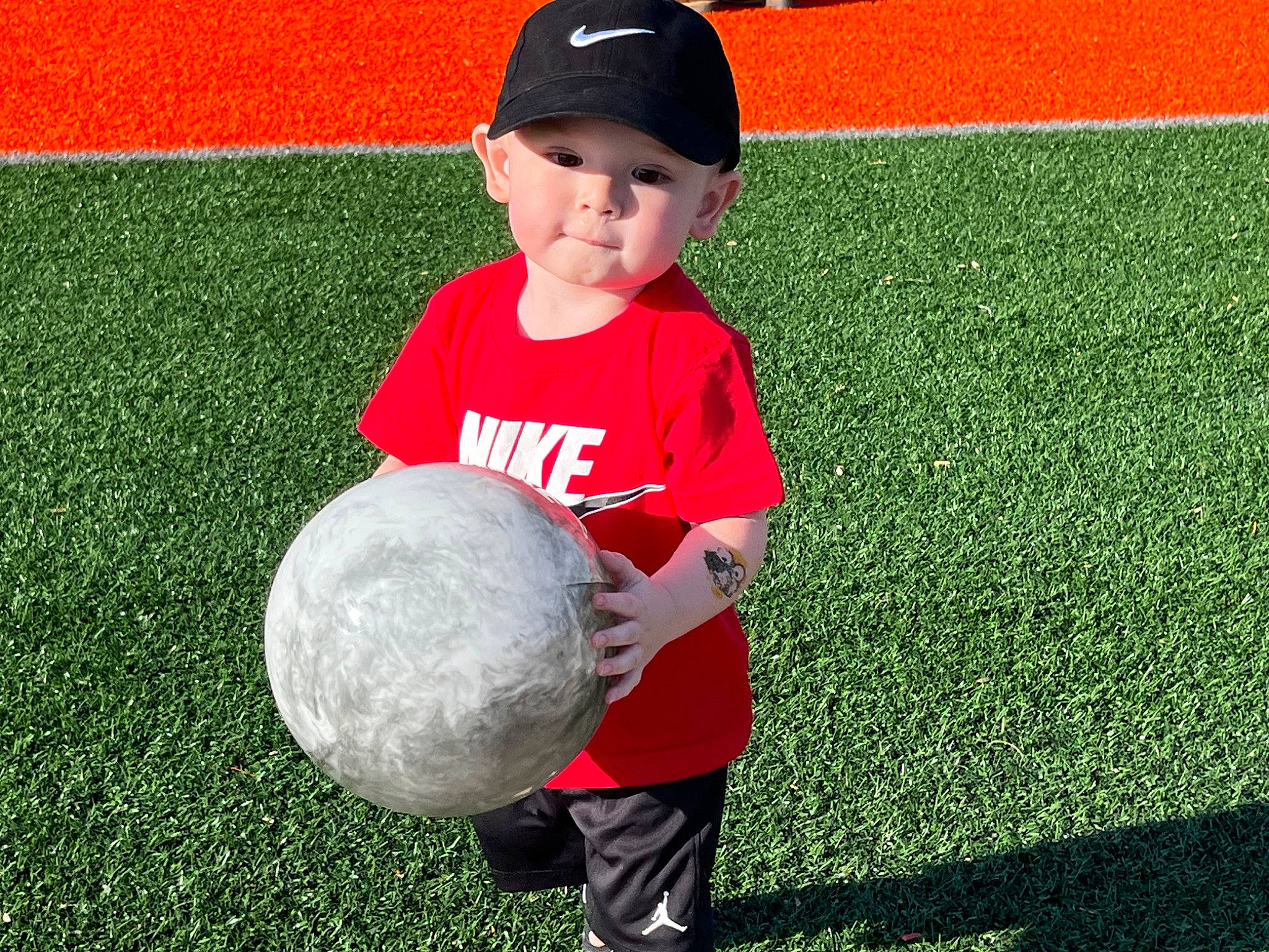 Kendan is registered to the contest to win money with this photo: ball, ball_game, baseball_cap, cap, flooring, fun, gesture, grass, happy, headwear, mammal, people_in_nature, person, player, playing_sports, smile, soccer_ball, sports, sports_toy, t_shirt