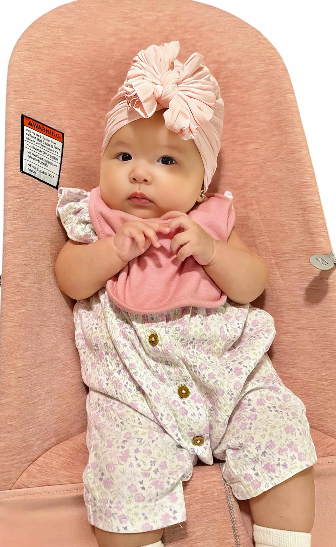 Isabella is registered to the contest to win money with this photo: baby, infant, child, pink, headwrap, bib, floral_outfit, baby_seat, cute, adorable, sitting, clothing, soft_texture, comfortable, portrait, face, hands, expression, indoor, earrings