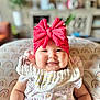 Isabella is registered to the contest to win money with this photo: baby, child, smiling, headband, red_bow, cheeks, cushion, rainbow_pattern, clothing, infant, portrait, indoors, cute, happy, sitting, soft_lighting, face, hand, apparel, home