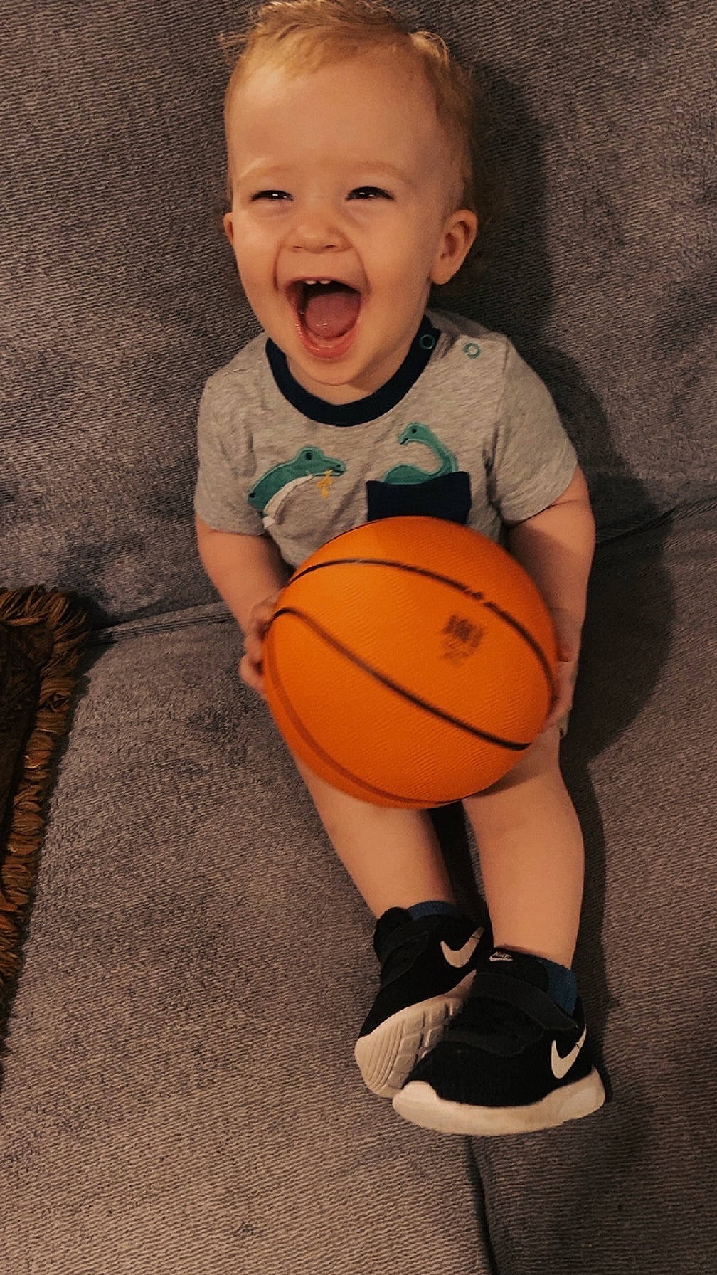 Sebastian is registered to the contest to win money with this photo: basketball, casual, child, clothing, couch, cute, dinosaur, footwear, happy, indoor, joyful, nike, orange, person, shoes, sitting, smile, toddler, toy, young_child