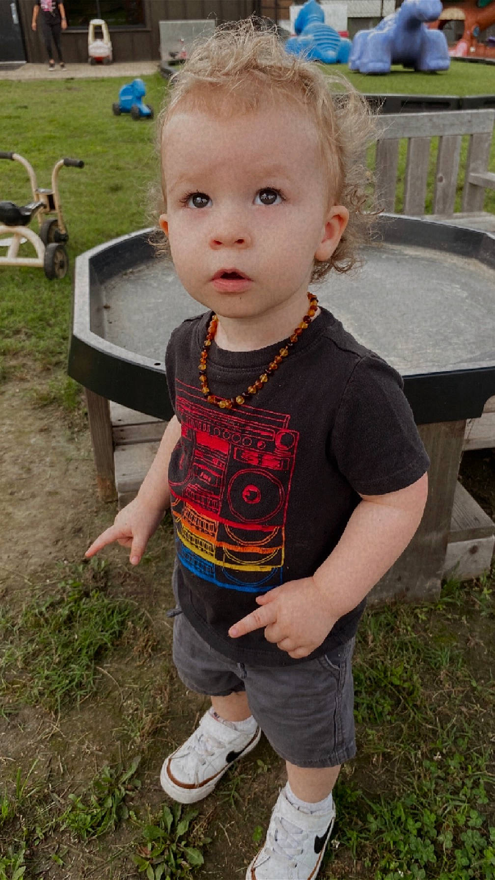 Sebastian joined the competition — help win amazing prizes! casual_clothing, child, curiosity, curly_hair, daylight, expression, grass, nature, necklace, outdoor, person, playground, pointing, shoes, shorts, toddler, toy, tshirt, wooden_bench, young_child