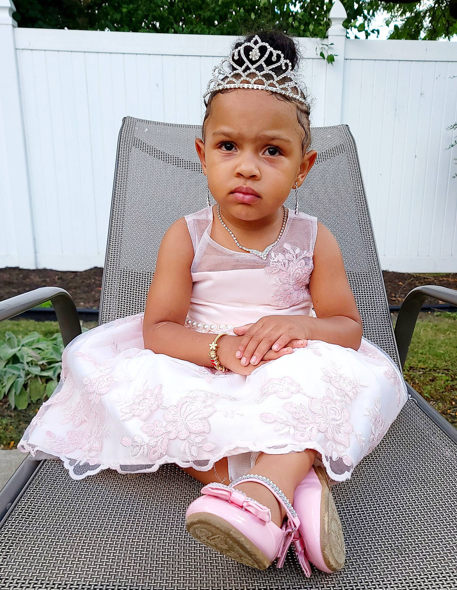 Alayah is registered to the contest to win money with this photo: baby_toddler_clothing, bridal_accessory, dress, embellishment, face, fashion_design, flash_photography, grass, happy, head, headpiece, headwear, jewellery, knee, neck, necklace, person, pink, plant, sleeve