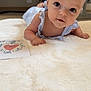 baby, infant, child, blue_clothing, fluffy_rug, indoor, card, heart, curious, lying_down, wide_eyes, soft_texture, portrait, close_up, floor, candid, cute, human, young, skin