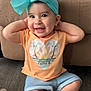 baby, barefoot, bow, child, clothing, couch, cute, denim_shorts, floor, hands, happy, head, headband, indoor, orange_tshirt, person, portrait, sitting, smiling, young_child