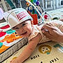 baby, infant, smiling, hat, paper_hat, play_mat, toy, hand, home, floor, colorful, cute, child, person, indoor, happy, reaching, clothing, support, face