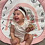 baby, child, smiling, sitting, headband, flower, onesie, wooden_toy, play_mat, numbers, pink, white, floral, floor, happy, indoors, cute, infant, person, portrait