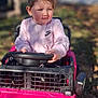 toddler, child, toy_car, pink, outdoor, play, pigtails, steering_wheel, sunlight, casual_clothing, nike_logo, grass, daylight, expression, person, young_child, vehicle, playtime, fun, nature