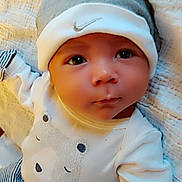 Steven is registered to the contest to win money with this photo: baby, infant, hat, clothing, cute, face, eyes, expression, lying_down, blanket, striped_pants, white_shirt, bear_design, headwear, soft_texture, heart_graphics, newborn, child, portrait, indoors