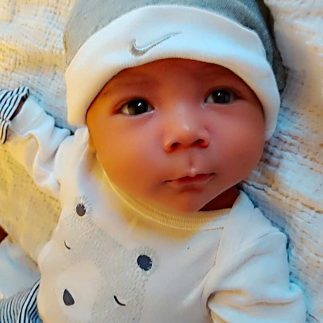 Steven is registered to the contest to win money with this photo: baby, infant, hat, clothing, cute, face, eyes, expression, lying_down, blanket, striped_pants, white_shirt, bear_design, headwear, soft_texture, heart_graphics, newborn, child, portrait, indoors