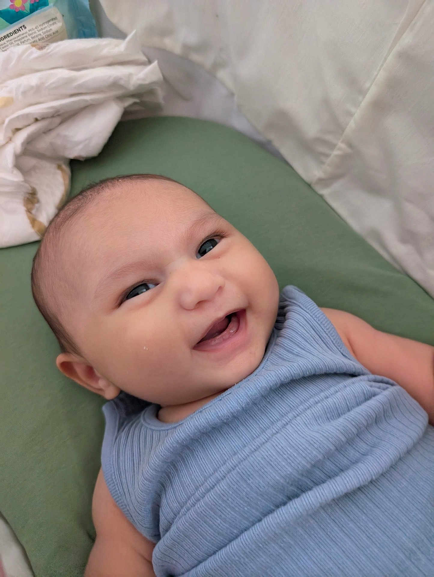 Eren joined the competition — help win amazing prizes! baby, smiling, infant, face, blue_clothing, cushion, green, lying_down, happy, skin, head, eyes, mouth, teeth, fabric, blanket, indoors, closeup, child, person