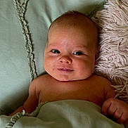 Noah is registered to the contest to win money with this photo: baby, infant, smile, blanket, pillow, face, skin, hand, lying_down, cute, indoors, cozy, child, young, soft_texture, expression, portrait, head, resting, comfort