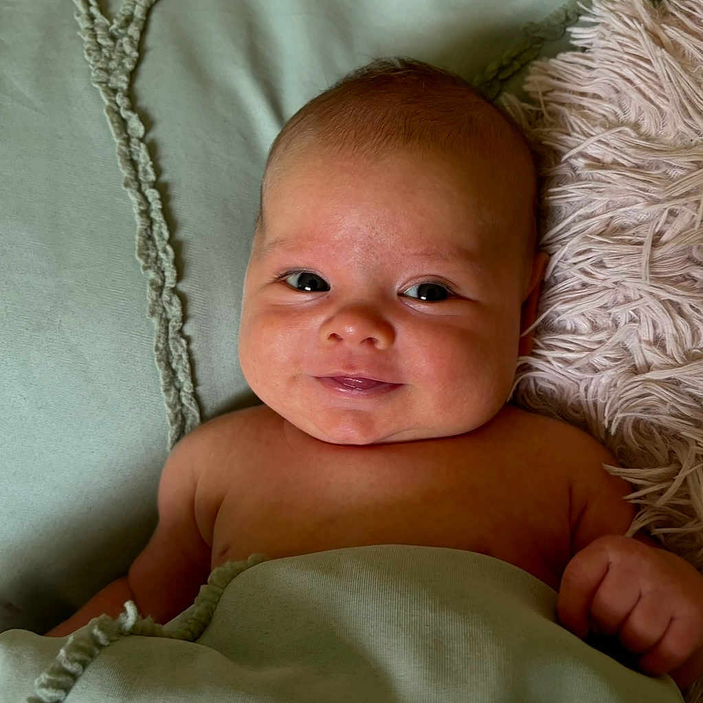 Noah is registered to the contest to win money with this photo: baby, blanket, child, comfort, cozy, cute, expression, face, hand, head, indoors, infant, lying_down, pillow, portrait, resting, skin, smile, soft_texture, young