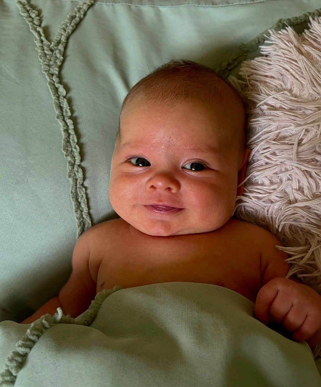Noah is registered to the contest to win money with this photo: baby, infant, smile, blanket, pillow, face, skin, hand, lying_down, cute, indoors, cozy, child, young, soft_texture, expression, portrait, head, resting, comfort