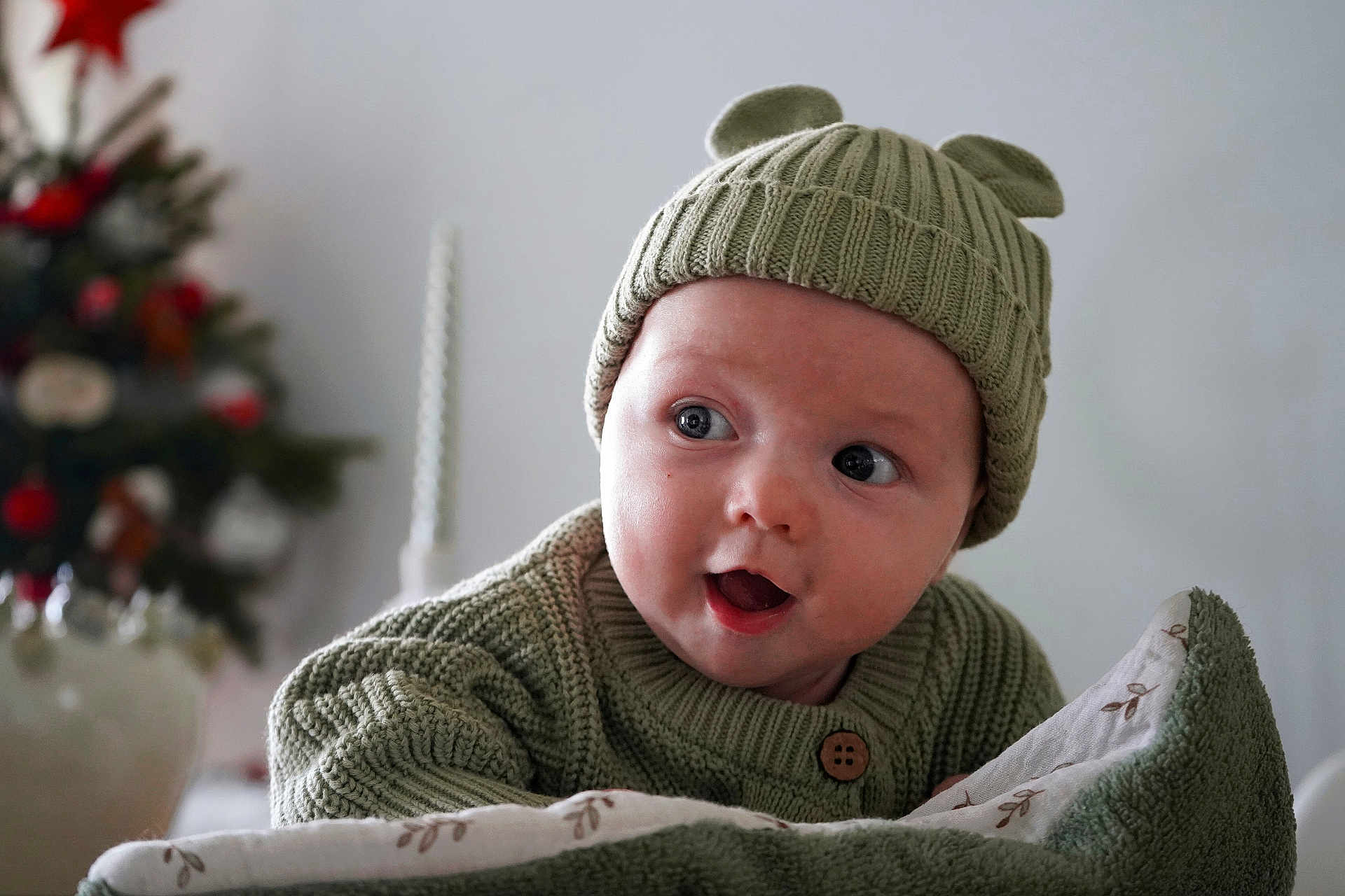 Gabin participe au concours pour gagner de l'argent avec cette photo : baby, child, knit_hat, green_sweater, blanket, face, wide_eyes, open_mouth, cute, indoor, christmas_tree, holiday, soft_texture, warm_clothing, portrait, infant, cozy, expression, decor, festive
