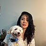 woman, dog, pet, portrait, indoor, white_dog, curly_hair, smiling_dog, casual_clothing, neutral_background, collar, tag, happy, holding_pet, face, long_hair, cute, friendly, companion, animal