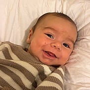 Eliot a rejoint le concours — aidez-le/la à gagner de superbes lots ! baby, smiling, cozy, striped_sweater, blanket, pillow, indoor, child, happy, cute, infant, portrait, lying_down, warm_colors, soft_texture, face, person, young_child, comfort, sleeping_area