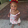 toddler, child, birthday_headband, smile, barefoot, dress, happy, standing, outdoor, floor, concrete, brick, person, cute, colorful, headwear, celebration, young_child, skin, eyes