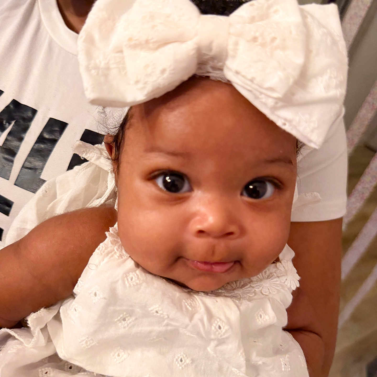 Anyla is registered to the contest to win money with this photo: baby, child, infant, white_bow, white_dress, curly_hair, wide_eyes, smile, person, indoor, holding, adult, face, portrait, closeup, cute, clothing, headwear, skin, expression