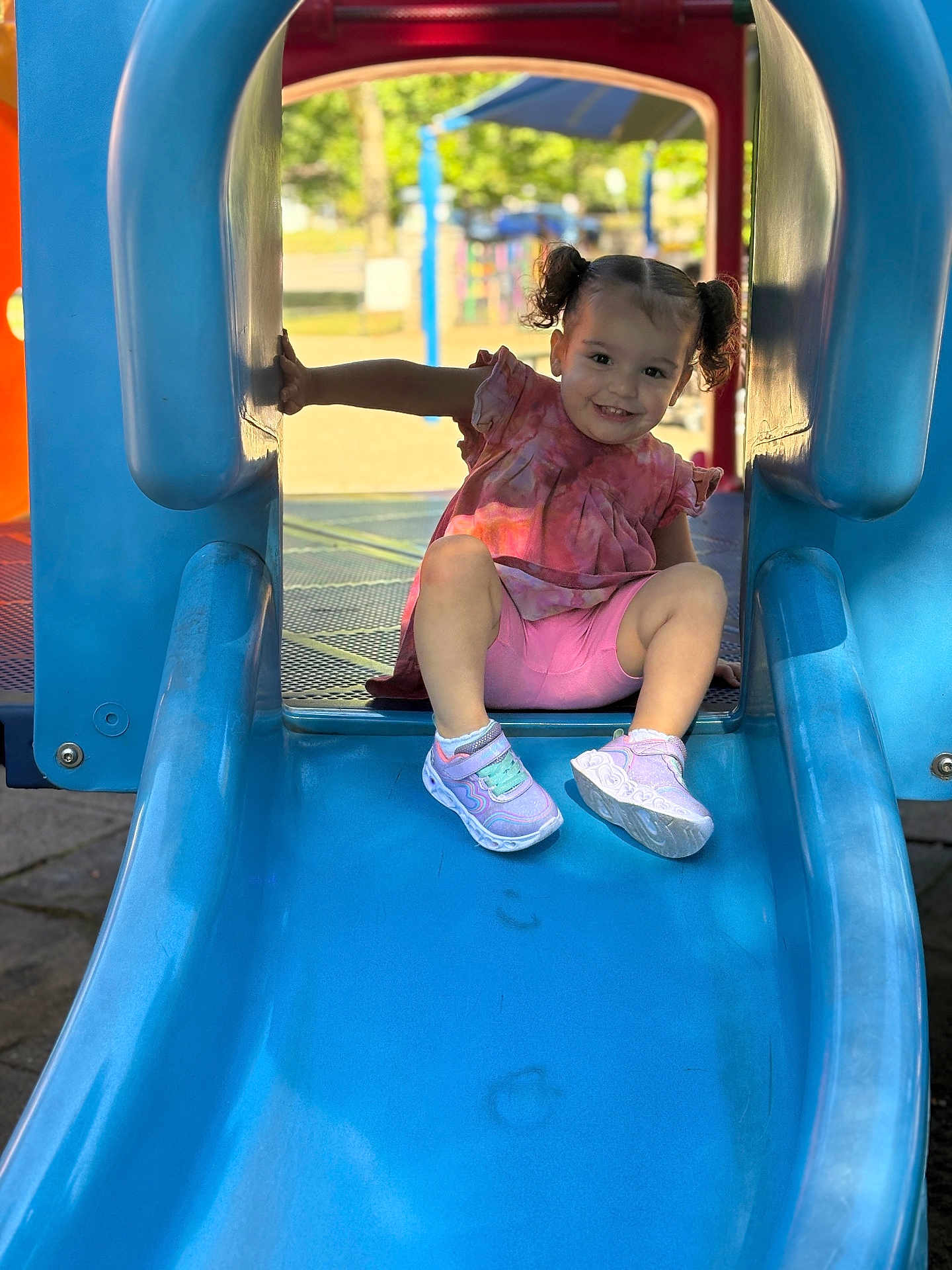 Celine joined the competition — help win amazing prizes! toddler, child, playground, slide, blue_slide, pink_clothing, pigtails, smiling, outdoor, daylight, park, recreation, fun, happy, shoes, casual_wear, play, person, cute, summer