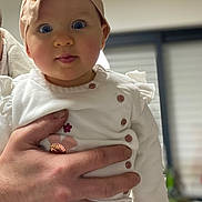 Olivia a rejoint le concours — aidez-le/la à gagner de superbes lots ! baby, infant, child, headband, pink, white_shirt, hand, holding, portrait, cute, indoors, person, face, eyes, clothing, blurred_background, expression, skin, fingers, toddler