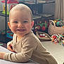baby, smile, blue_eyes, toys, indoor, child, happy, sweater, furniture, shelf, playroom, curious, leaning, soft_surface, cute, portrait, infant, home, colorful, young_child