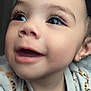 baby, close_up, smiling, happy, face, eyes, eyelashes, mouth, cheeks, clothing, patterned_clothing, earring, curly_hair, infant, cute, portrait, child, indoor, soft_light, joy