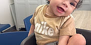Kiari Bennett is registered to the contest to win money with this photo: toddler, child, smiling, baby_seat, nike_tshirt, curly_hair, indoor, table, locker, chair, happy, playful, person, furniture, seatbelt, skin, foot, hand, cute, portrait