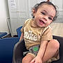 toddler, child, smiling, baby_seat, nike_tshirt, curly_hair, indoor, table, locker, chair, happy, playful, person, furniture, seatbelt, skin, foot, hand, cute, portrait