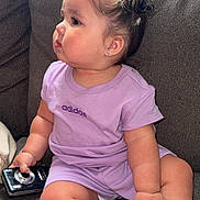 Itzayana is registered to the contest to win money with this photo: adidas, baby, barefoot, camera, casual, child, chubby, couch, curly_hair, cute, earrings, furniture, gray_couch, indoor, person, purple_clothing, side_profile, sitting, sunlight, toddler