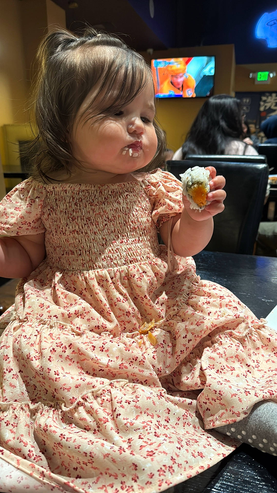 Itzayana joined the competition — help win amazing prizes! apparel, background, child, cute, dining, dress, face, floral, food, hair, indoor, messy, people, person, restaurant, rice, seated, sushi, table, toddler
