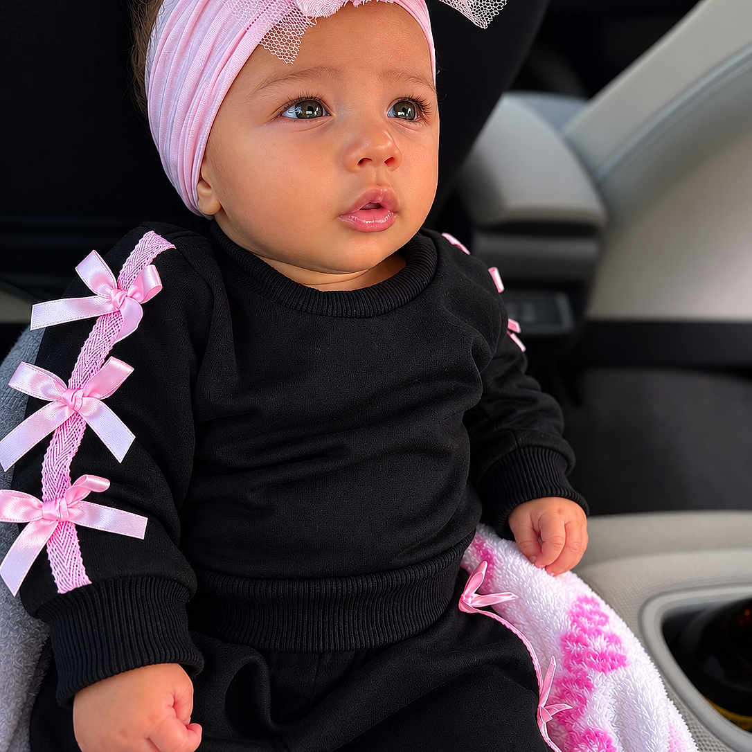 Mia Sophia Barrera is registered to the contest to win money with this photo: baby, child, infant, black_clothing, pink_bows, headband, flower, car_seat, blanket, pink_and_white, cute, portrait, indoors, small_hand, curious_expression, sitting, face, eyes, lips, cozy