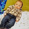 baby, child, plaid_shirt, denim_jeans, bed, pillow, blanket, floral_pattern, indoor, person, cute, toddler, casual_clothing, foot, lying_down, resting, young_child, soft_lighting, portrait, cozy
