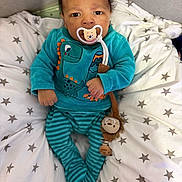 Fodé a rejoint le concours — aidez-le/la à gagner de superbes lots ! baby, infant, pacifier, plush_toy, dinosaur_outfit, striped_pants, star_pattern, cushion, blanket, blue_clothing, cozy, cute, indoor, child, person, lying_down, comfortable, soft_toys, face, young