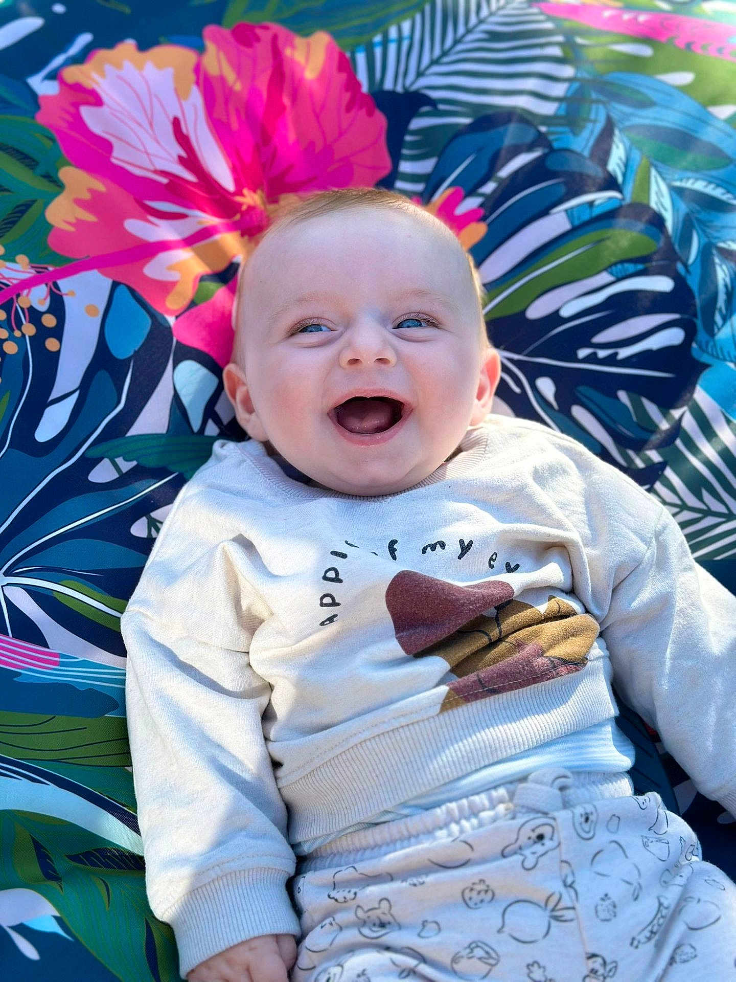 Paul a rejoint le concours — aidez-le/la à gagner de superbes lots ! baby, smiling, blue_eyes, sweatshirt, pants, patterned_clothing, tropical_blanket, colorful, happy, child, infant, portrait, outdoor, sunlight, cute, joyful, lying_down, closeup, face, expression