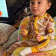 Eden is registered to the contest to win money with this photo: toddler, child, onesie, colorful_blanket, indoor, television, furniture, smiling, cute, face, sitting, sock, plush, patterned_clothing, living_room, toy, cozy, home, yellow, playful