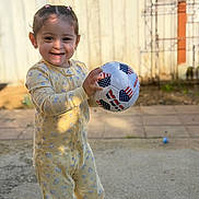 Paisley joined the competition — help win amazing prizes! toddler, child, smile, soccer_ball, ball, pajamas, yellow_pajamas, outdoor, backyard, fence, sunlight, bokeh, portrait, standing, happy, play, concrete, hair_ties, earrings, daylight