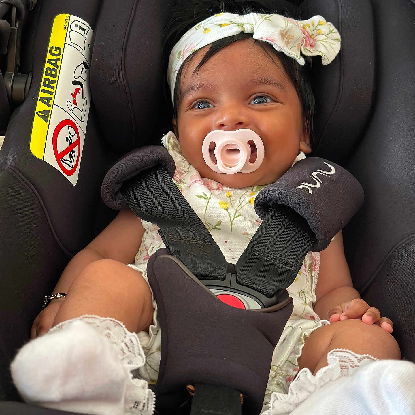 Mya is registered to the contest to win money with this photo: baby, car_seat, child, closeup, clothing, cute, floral_pattern, footwear, happy, headband, indoors, infant, pacifier, person, portrait, safety, seat_belt, smiling, straps, white_socks