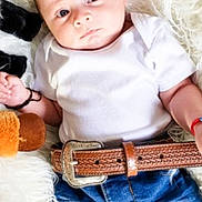 Megan joined the competition — help win amazing prizes! baby, infant, child, white_onesie, blue_jeans, brown_belt, plush_toy, fluffy_blanket, lying_down, cute, curious, indoor, portrait, small_hands, soft_texture, young_child, casual_clothing, human, face, blue_eyes
