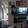 cat, lamp, table, television, wall_art, living_room, floor_tile, hallway, chair, sofa, door, decor, window_blinds, book, bottle, tissue_box, electronic_device, poster, cable, shadow