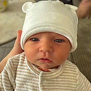 Sacha participe au concours pour gagner de l'argent avec cette photo : baby, infant, child, face, hat, clothing, onesie, hand, indoor, portrait, cute, serious, soft_lighting, blurred_background, table, striped, white_hat, newborn, person, closeup