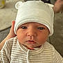 baby, infant, child, face, hat, clothing, onesie, hand, indoor, portrait, cute, serious, soft_lighting, blurred_background, table, striped, white_hat, newborn, person, closeup