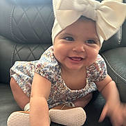 Kelsey is registered to the contest to win money with this photo: baby, infant, smiling, headband, bow, dress, floral_pattern, crawling, shoes, leather_chair, cute, happy, child, indoors, person, apparel, footwear, tongue, hand, skin