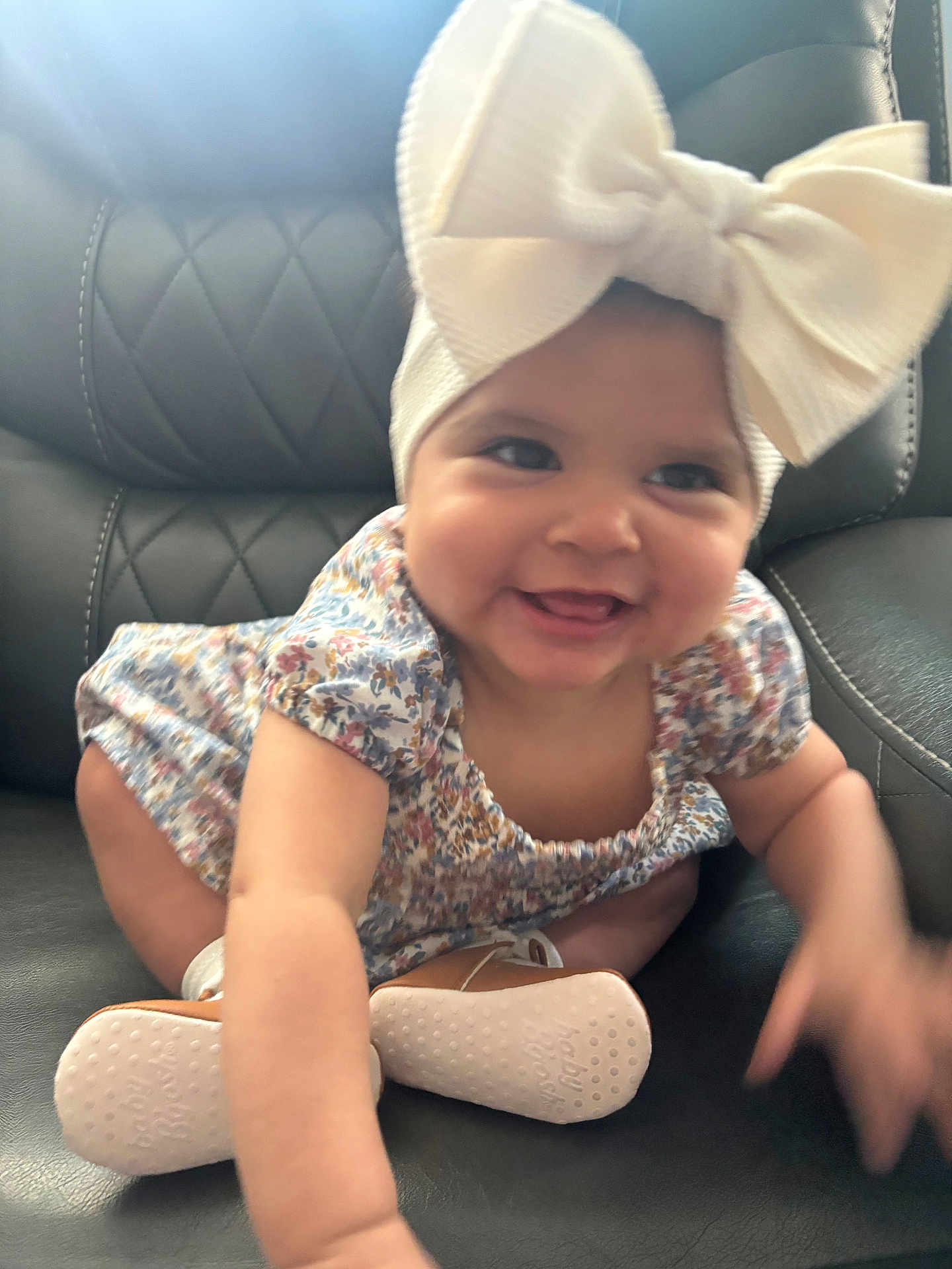 Kelsey is registered to the contest to win money with this photo: baby, infant, smiling, headband, bow, dress, floral_pattern, crawling, shoes, leather_chair, cute, happy, child, indoors, person, apparel, footwear, tongue, hand, skin