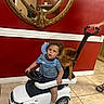 toddler, toy_car, dog, indoor, red_wall, mirror, mirror_frame, hand, footwear, tile_floor, child, pet, seat, person, furniture, foot, clothing, socks, play, vehicle