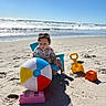 Christopher is registered to the contest to win money with this photo: toddler, beach, sand, beach_ball, blue_chair, yellow_shovel, orange_sand_mold, pink_sand_mold, ocean, waves, sunny, sky, child, playing, summer, outdoor, toy, footprints, sunglasses, casual_clothing