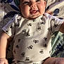 baby, infant, smiling, onesie, bee_pattern, cute, happy, tongue_out, lying_down, blanket, floral_pattern, child, skin, face, head, arm, leg, indoors, soft_lighting, person
