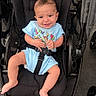 Easton is registered to the contest to win money with this photo: baby, child, stroller, smiling, blue_clothing, play_time, seatbelt, infant, cute, tongue_out, black_stroller, outdoor, happy, person, legs, skin, head, short_hair, baby_clothes, cartoon_print