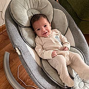 Easton is registered to the contest to win money with this photo: baby, infant, smile, onesie, baby_rocker, cushion, wooden_floor, indoor, person, furniture, happy, seat, head, face, cozy, baby_clothing, child, relax, living_room, cute